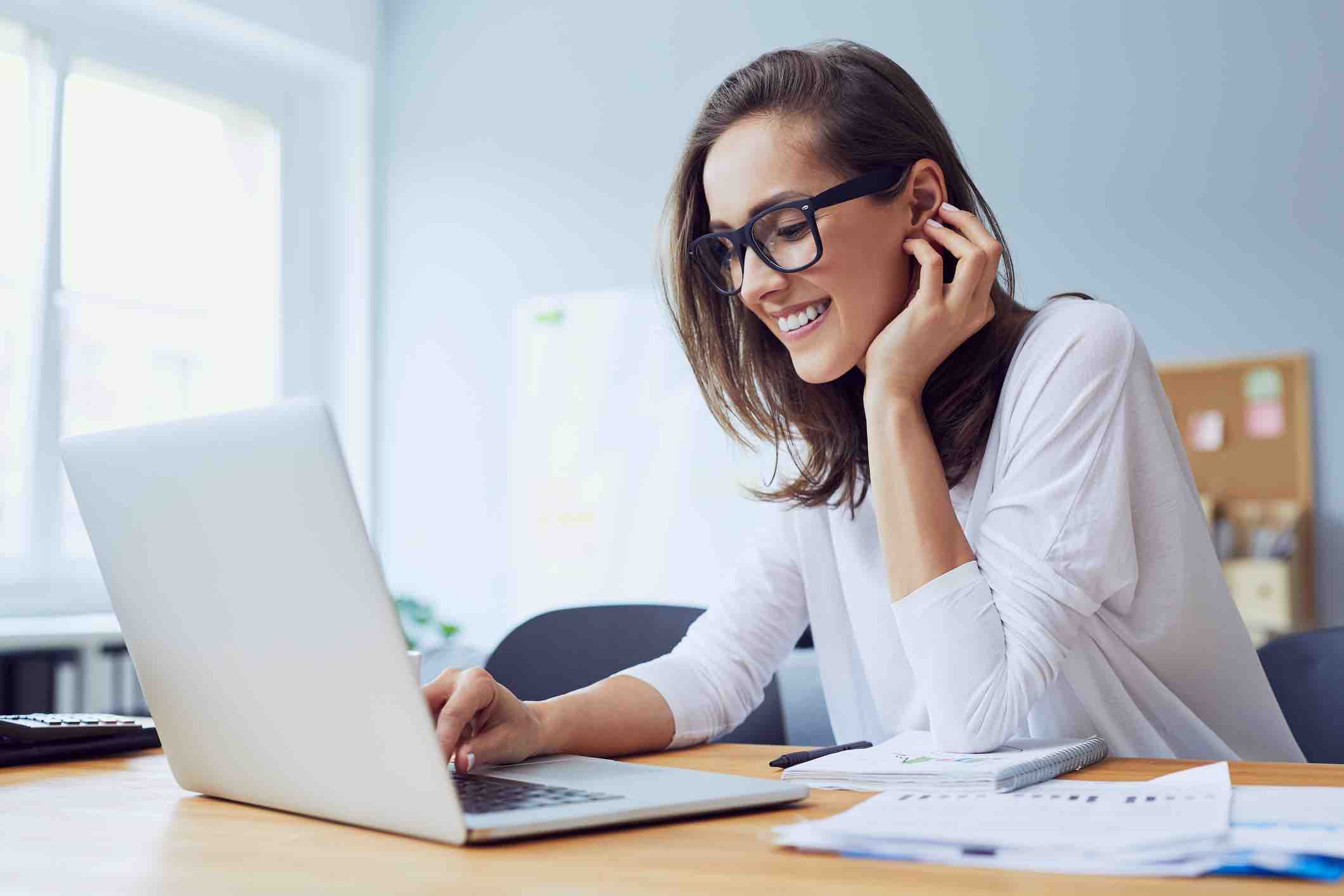 Portrait of beautiful cheerful young businesswoman working on laptop and laughing in home office